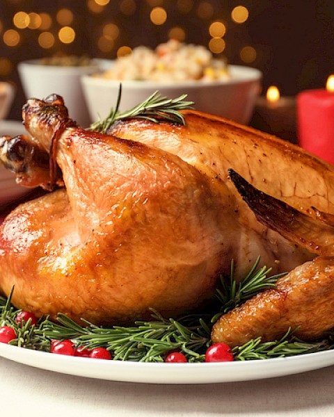 A roasted turkey garnished with rosemary and cranberries is surrounded by various side dishes on a festive dining table.