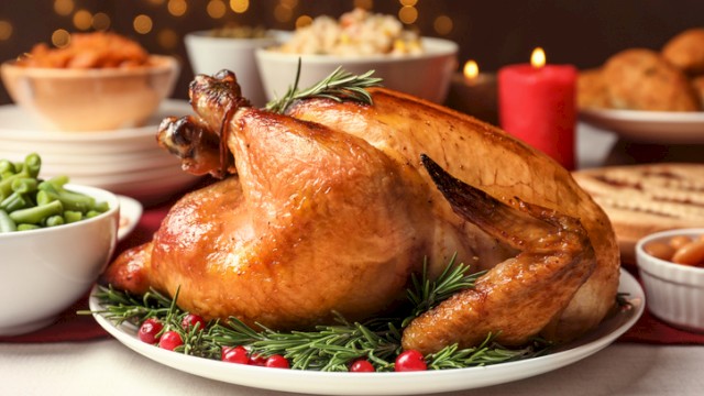 A roasted turkey garnished with rosemary and cranberries is surrounded by various side dishes on a festive dining table.