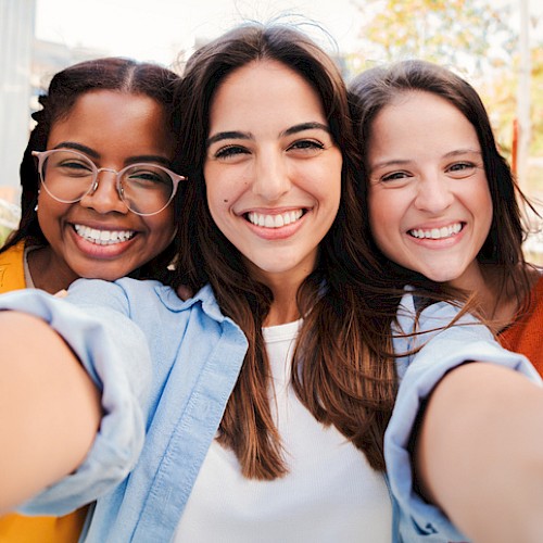 Three friends smiling for a selfie, happy and close, capturing a sunny day and good vibes.