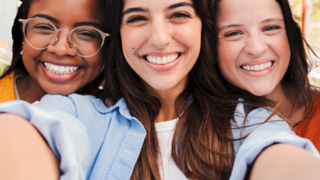 Three friends smiling for a selfie, happy and close, capturing a sunny day and good vibes.