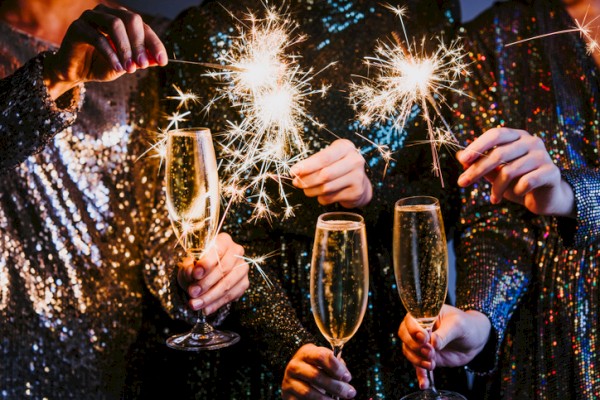 People celebrate with sparkling wine and lit sparklers, toasting together as night-time party lights.