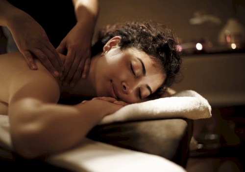 A person relaxing face down while receiving a massage in a dim spa setting.