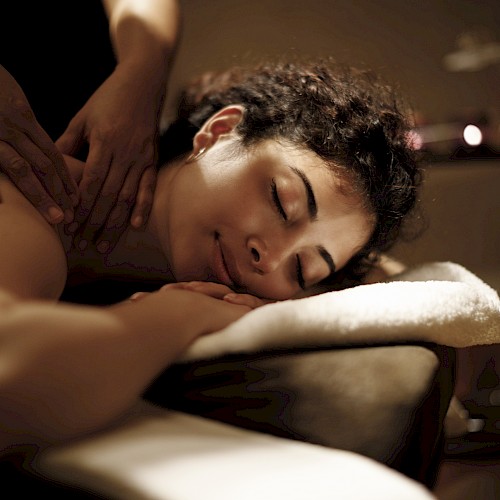 A person relaxing face down while receiving a massage in a dim spa setting.