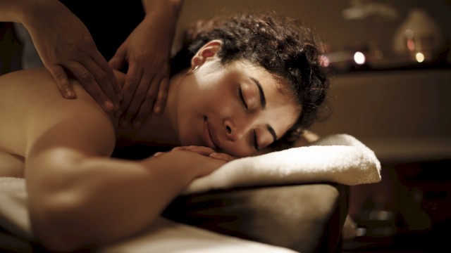 A person relaxing face down while receiving a massage in a dim spa setting.