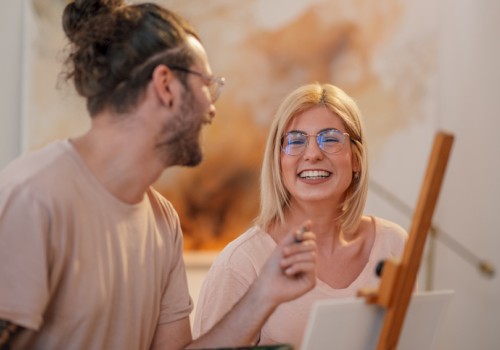 Two friends painting together, smiling and chatting in a cozy studio, sharing a moment of creativity and laughter as they work on a canvas.