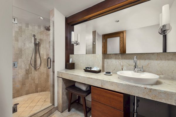A modern bathroom features a glass-enclosed shower, a large mirror, a countertop sink, and wooden accents throughout the design.