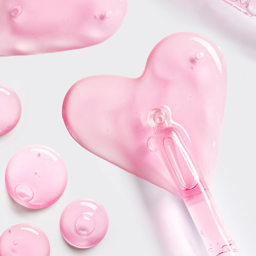 Two pink heart-shaped soaps or gels with a clear pink dropper, glossy and soft, on a light background, playful and dreamy.