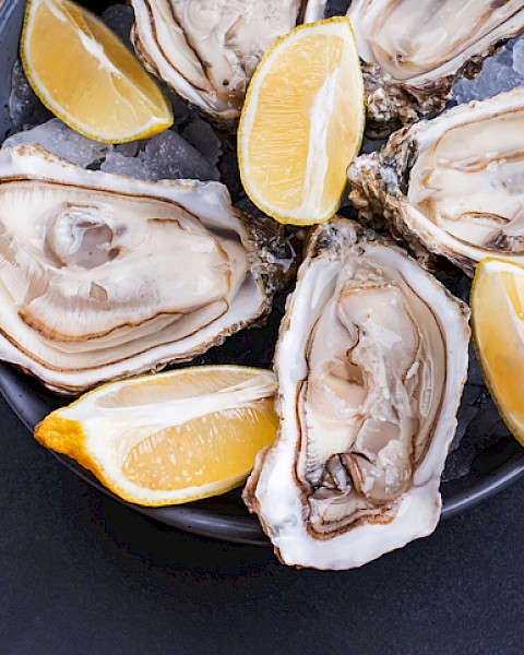 Fresh oysters with lemon wedges on a dark plate, ready to be enjoyed.