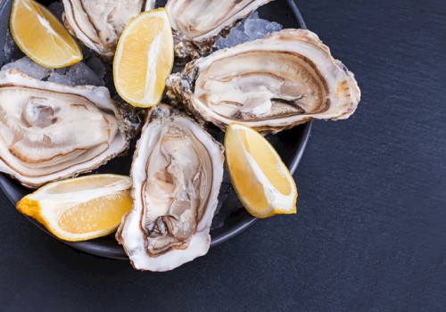 Fresh oysters with lemon wedges on a dark plate, ready to be enjoyed.