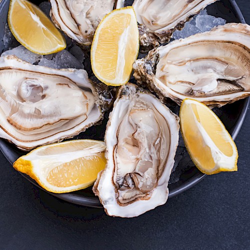Fresh oysters with lemon wedges on a dark plate, ready to be enjoyed.