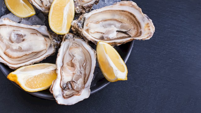 Fresh oysters with lemon wedges on a dark plate, ready to be enjoyed.