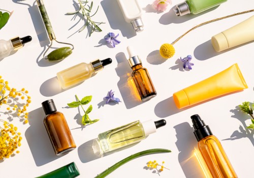 The image shows various skincare and beauty product bottles and tubes among flowers and greenery on a white background.