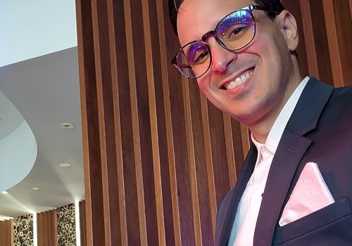 The image shows a person in a suit with glasses, smiling in a stylish setting with wood paneling and leopard print details on the walls.