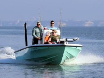 A motorboat is speeding across the water with three individuals on board, enjoying a day on the lake or sea.