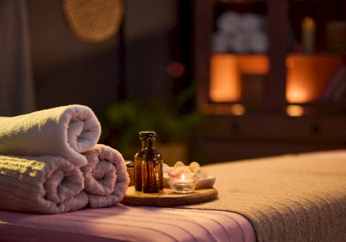 A neatly made massage table with soft towels, candles, and bottles, set in a cozy, dimly lit spa or massage room for relaxation.
