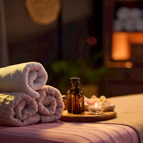A neatly made massage table with soft towels, candles, and bottles, set in a cozy, dimly lit spa or massage room for relaxation.