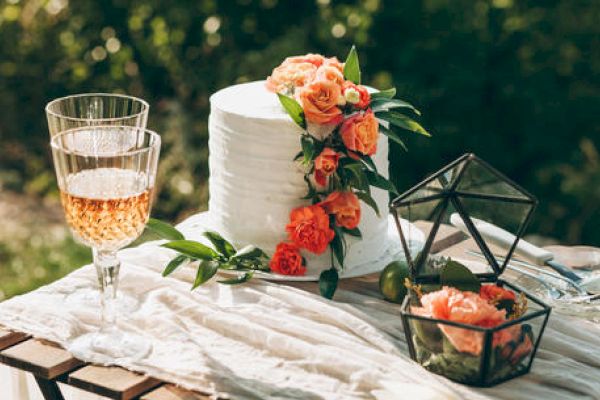 A beautifully decorated table with a white cake adorned with orange roses, a couple of glasses with a drink, and a geometric terrarium holding flowers.