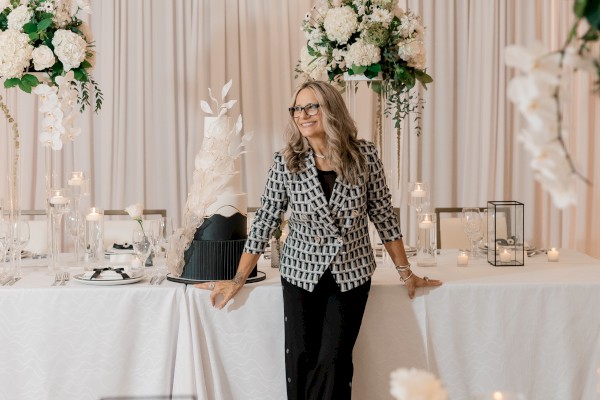 A person stands beside a decorated table with flowers, candles, and a cake in a well-lit event setting.