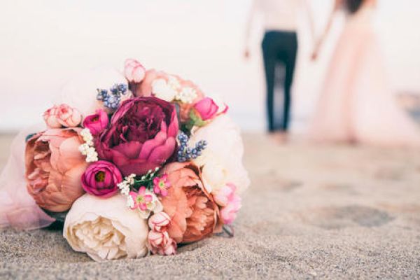 A bouquet of flowers is lying on the sand while a couple holding hands walks away in the background.