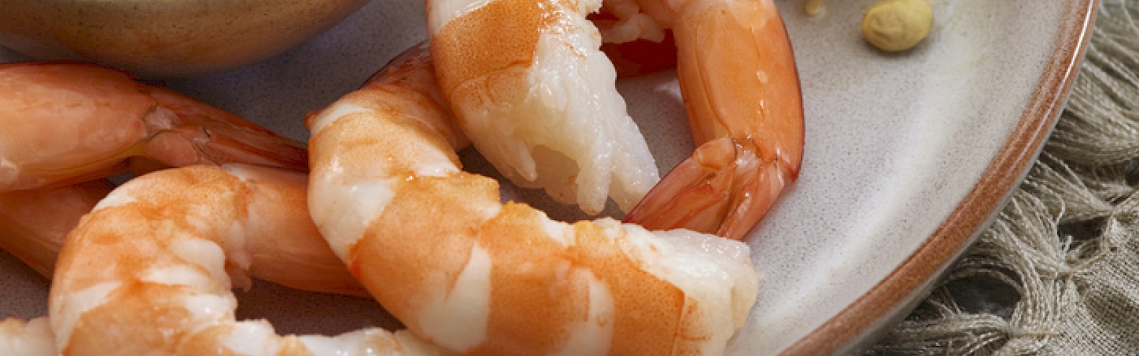 Cooked shrimp with lemon, herbs, and a side of tomato-based dipping sauce on a plate.