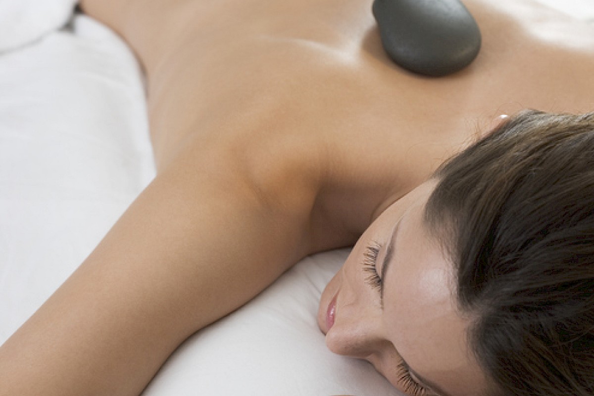 A woman is receiving a hot stone massage on her back in a spa setting.