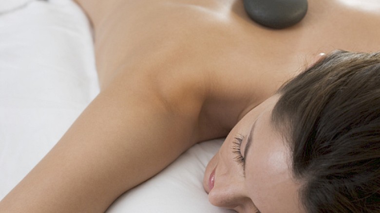 A woman is receiving a hot stone massage on her back in a spa setting.