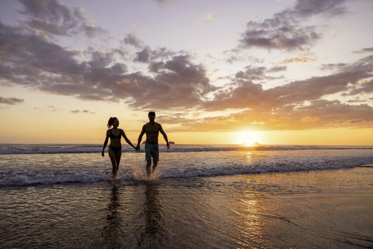 A couple walks hand in hand at the beach during sunset, creating a romantic and peaceful scene along the shoreline.