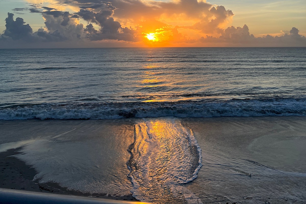 A peaceful sunset over the ocean with clouds and gentle waves reflecting the warm colors of the setting sun.