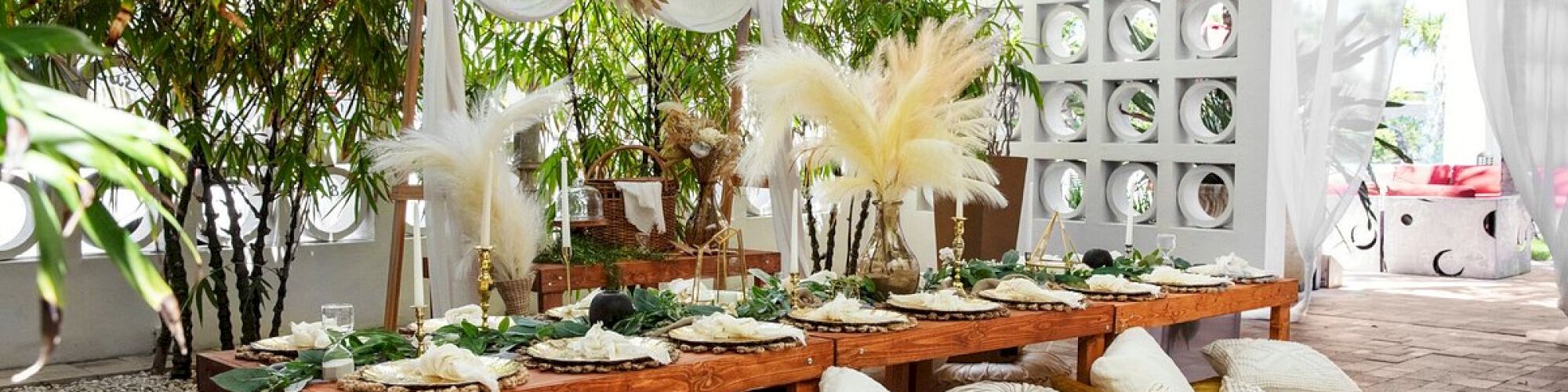An elegant outdoor dining setup with a low wooden table, cushions, plants, and decorative feathers, creating a cozy and serene ambiance.