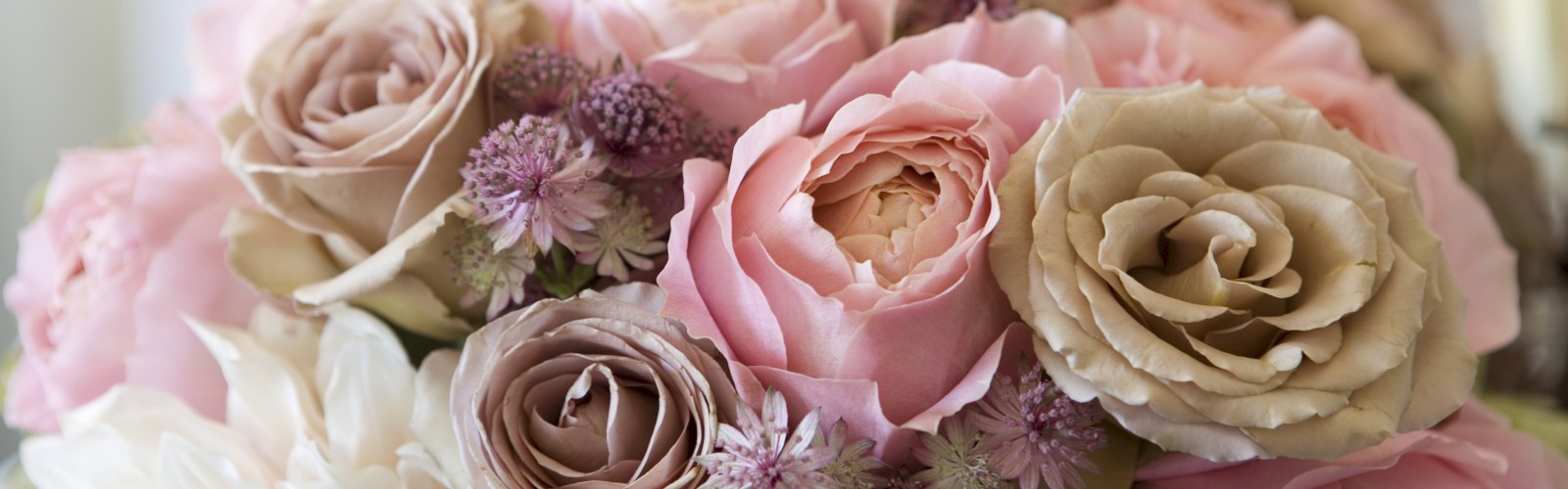 A bouquet of roses and various flowers in soft pink and beige tones, arranged closely together with a blurred background.