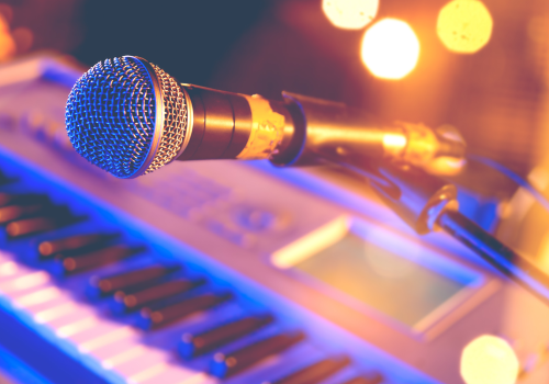 A microphone on a stand is positioned in front of an electronic keyboard, with vibrant orange and purple lighting in the background.