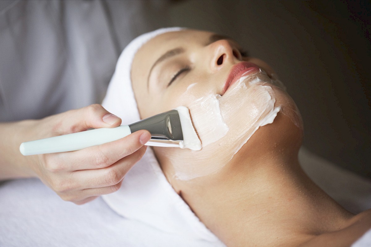 A woman is getting a facial treatment with a mask applied by a skincare professional for relaxation and skin care.