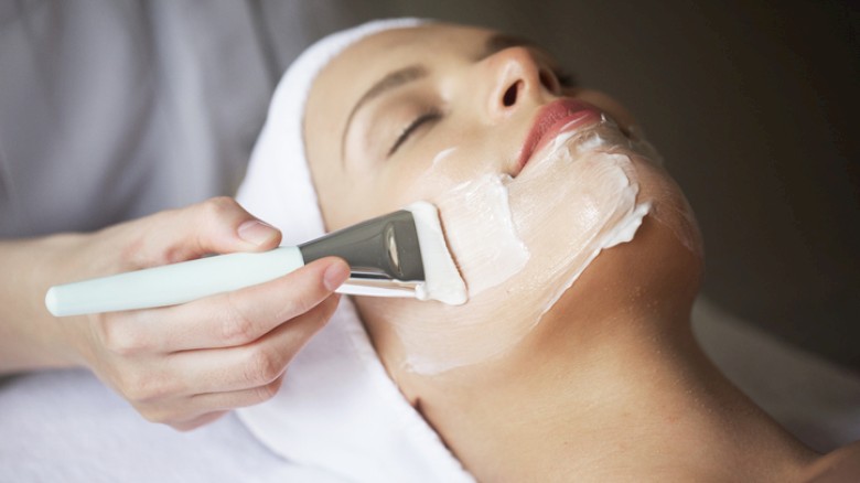 A woman is getting a facial treatment with a mask applied by a skincare professional for relaxation and skin care.