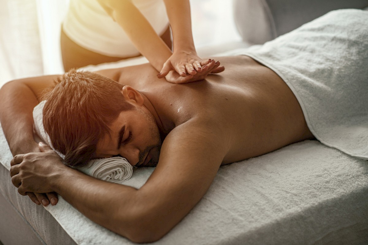 A man receives a back massage while lying face down on a massage table in a relaxing spa setting.