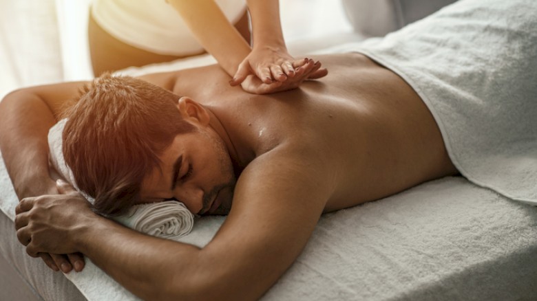 A man receives a back massage while lying face down on a massage table in a relaxing spa setting.