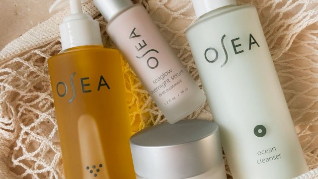 It shows a collection of Osea skincare products, including body oil, serum, cleanser, and protection cream, arranged in a net pouch on a textured surface.