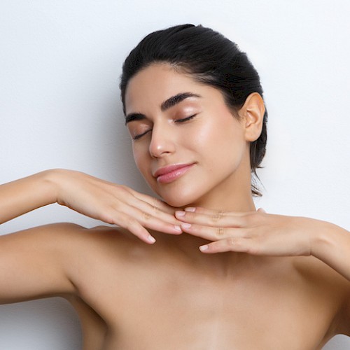 A woman with clear skin and closed eyes gently touches her face and neck, embodying relaxation and self-care.