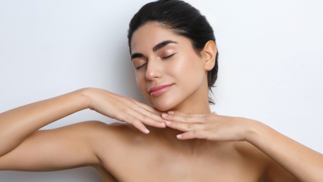A woman with clear skin and closed eyes gently touches her face and neck, embodying relaxation and self-care.