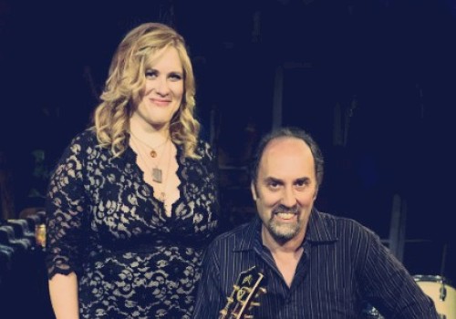 A woman in a black lace dress and a man holding a guitar at a music event.