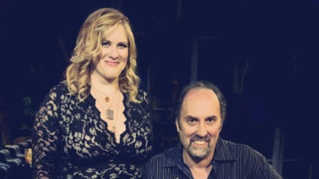 A woman in a black lace dress and a man holding a guitar at a music event.