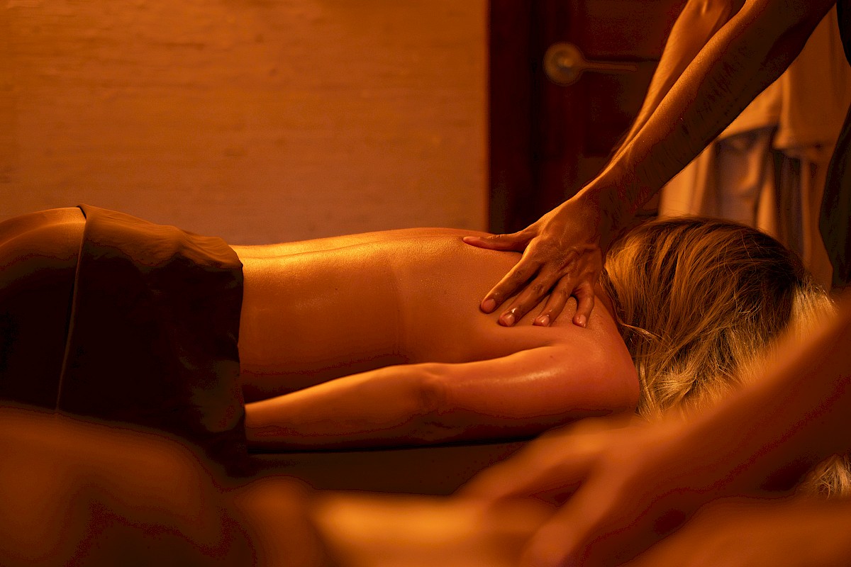 A person receives a massage on their back from a massage therapist in a warmly lit room.