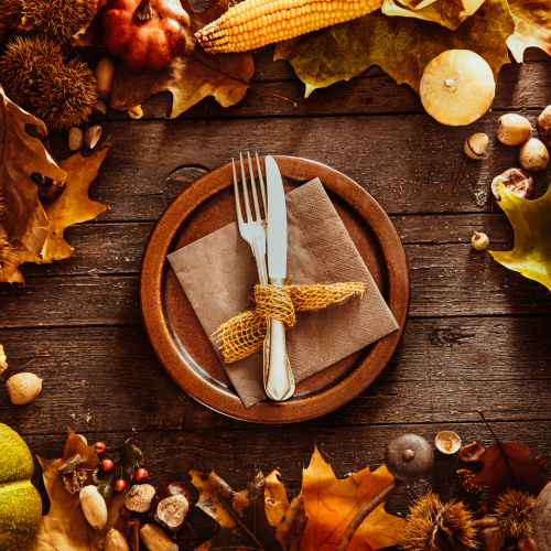 A rustic autumn table setting with a plate, utensils, corn, pumpkins, leaves, and nuts, creating a warm, seasonal atmosphere.