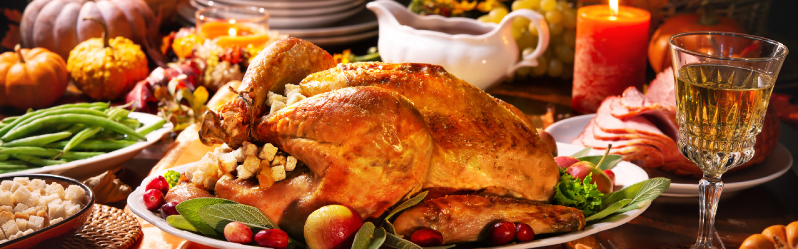 A festive table with a roasted turkey, pie, green beans, and wine, surrounded by pumpkins and candles for a Thanksgiving celebration.