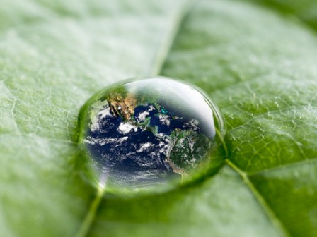 A water droplet on a green leaf reflects the Earth, symbolizing environmental awareness and our planet's fragility.