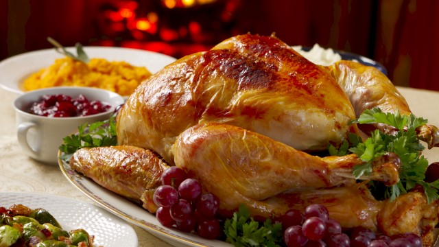A roasted turkey garnished with grapes, parsley, and an assortment of sides, including mashed potatoes, cranberry sauce, and vegetables, in front of a fire.