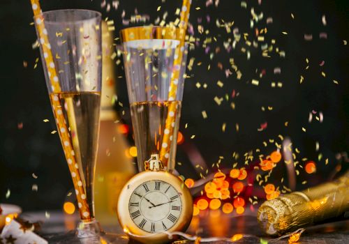 The image shows two champagne flutes with confetti, a pocket watch, and a champagne bottle, creating a celebratory atmosphere.