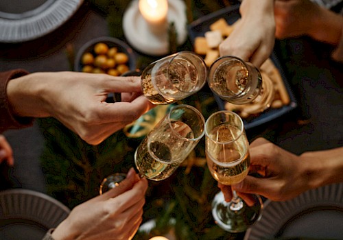 Friends toasting with champagne over a candlelit holiday table adorned with greenery, gifts, and festive decor.