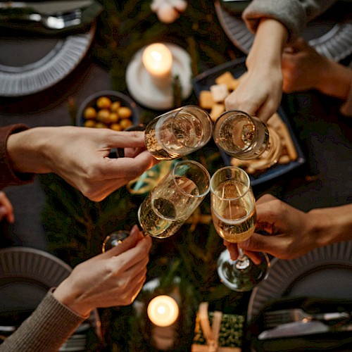 Friends toasting with champagne over a candlelit holiday table adorned with greenery, gifts, and festive decor.