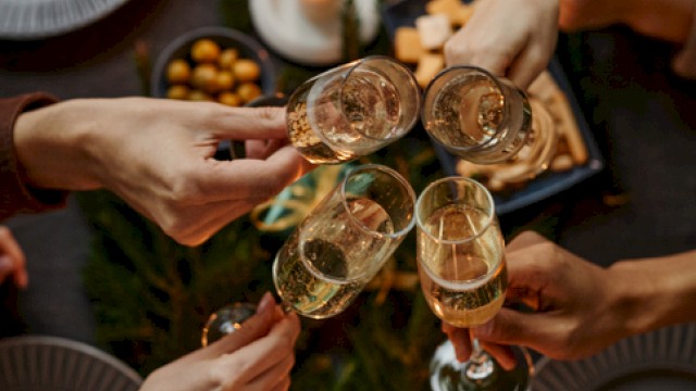 Friends toasting with champagne over a candlelit holiday table adorned with greenery, gifts, and festive decor.