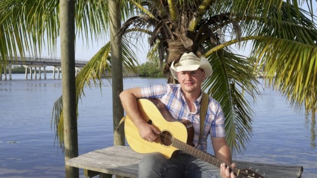 Man sitting on a picnic table with a cowboy hat and a guitar